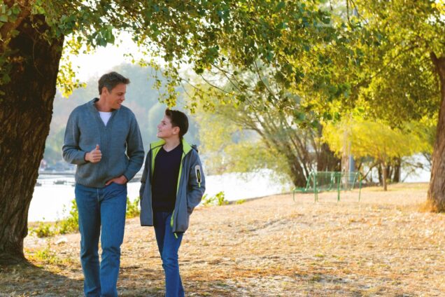 A young boy and a man walking together in a park talking