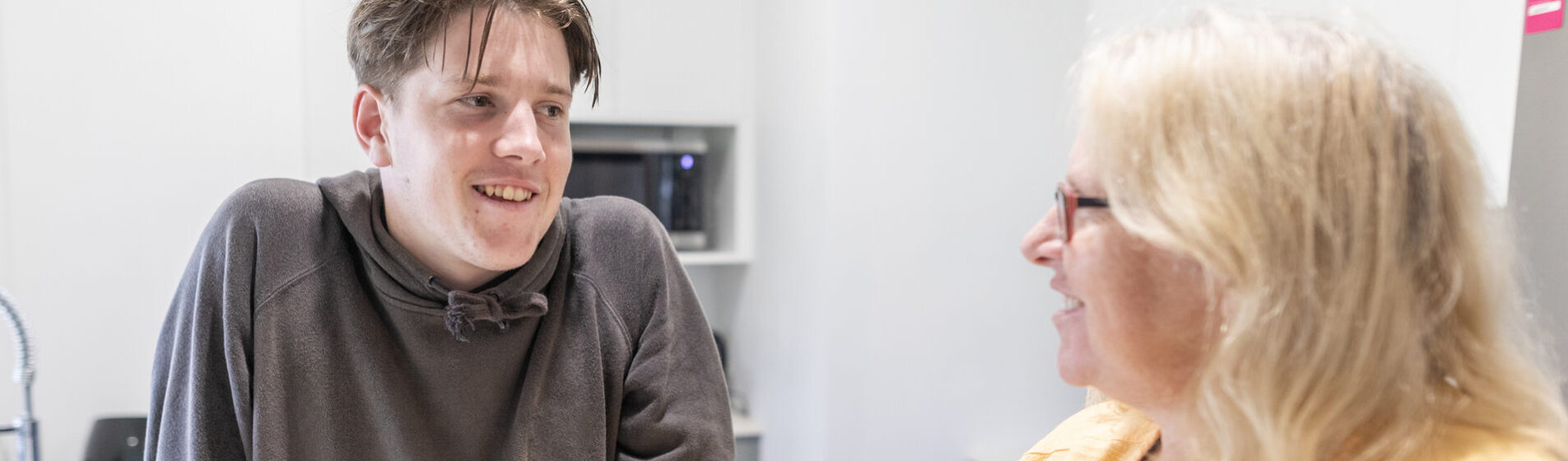 Young male with female foster care smiling and chatting in a kitchen