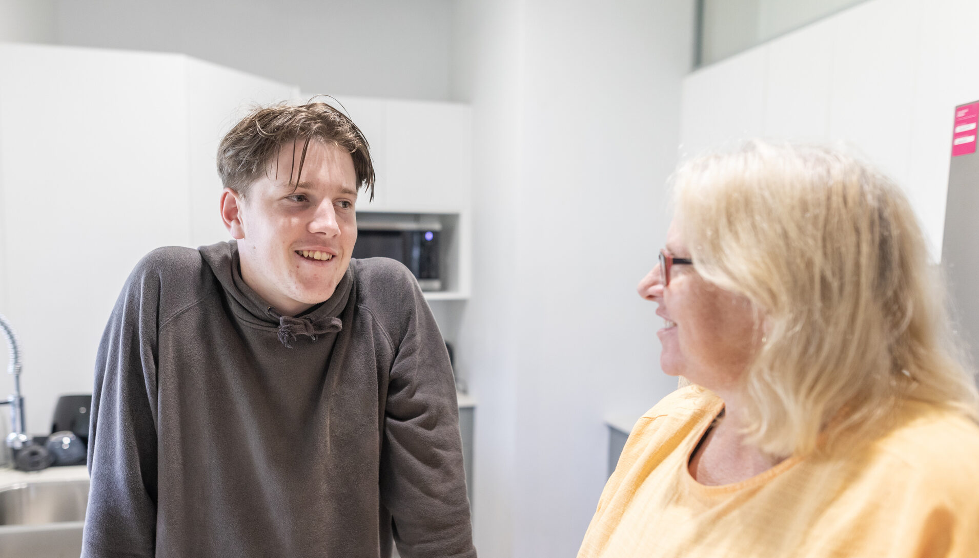 Young male with female foster care smiling and chatting in a kitchen
