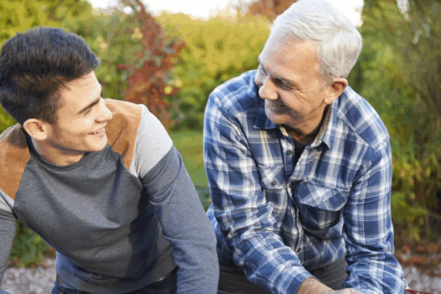 A teenage boy and a man sitting outside talking and laughing