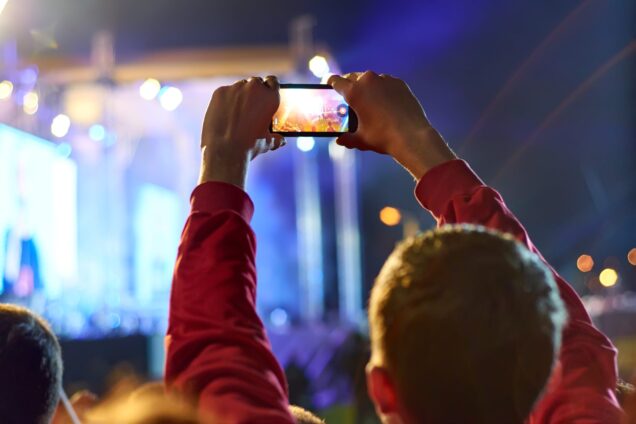 A man holding up his phone camera to record a concert