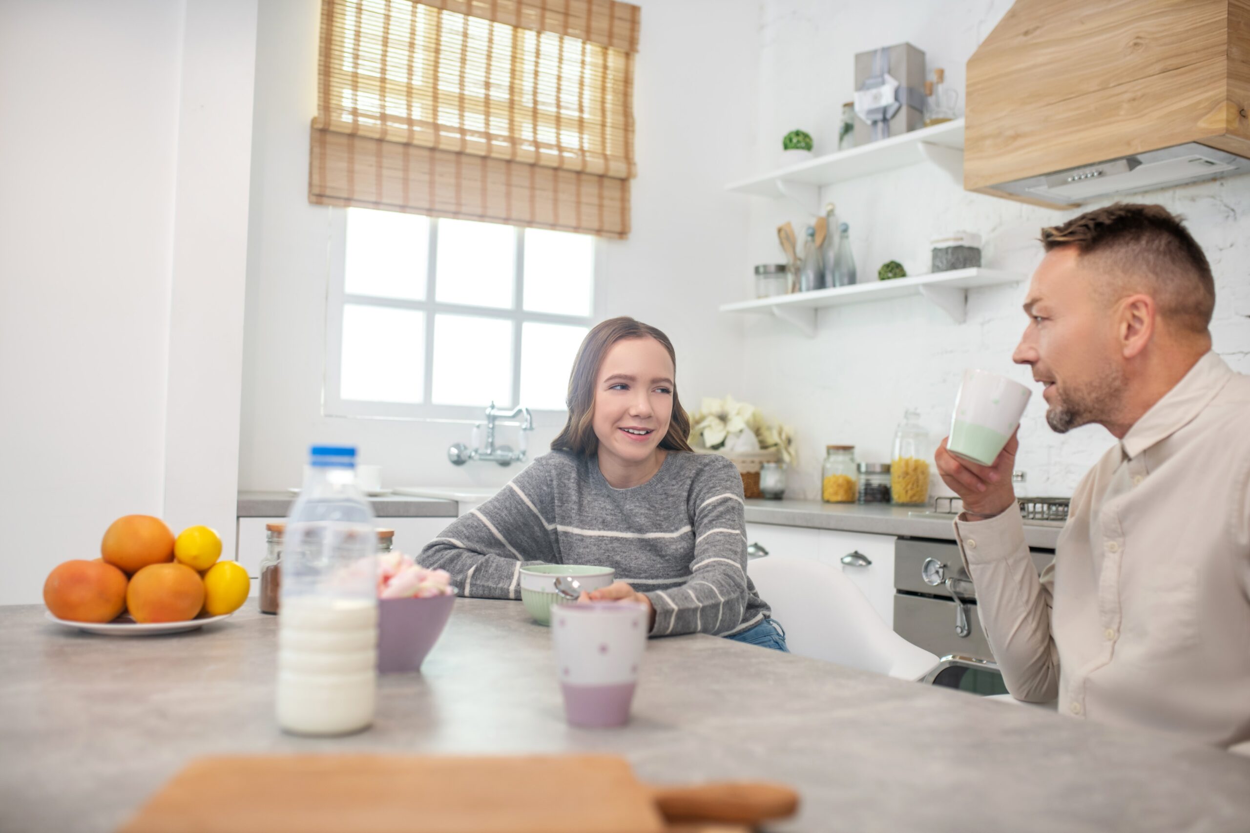 Teenage girl and male Foster Carer chatting at a table having breakfast