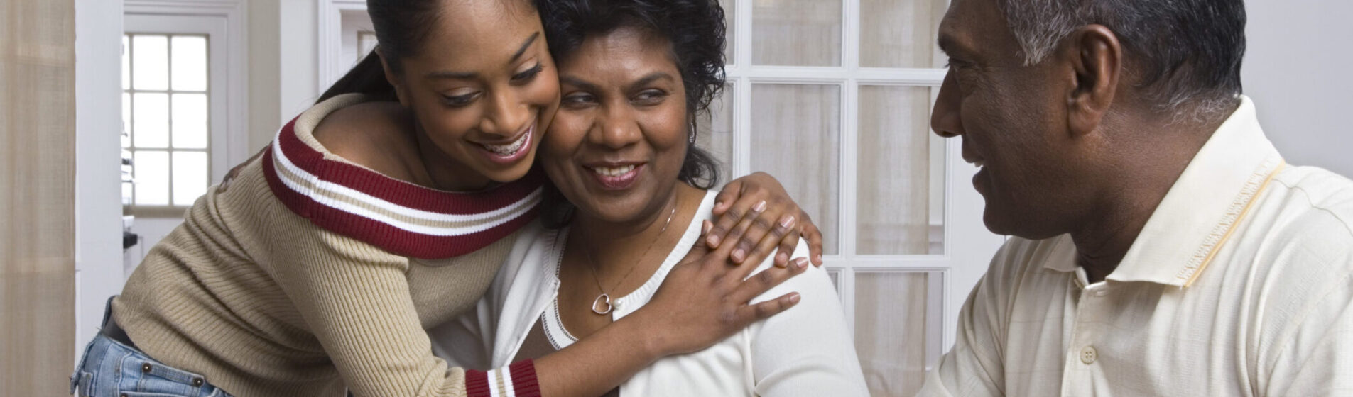 Young Person hugging her mother whilst looking at her father- everyone is happy