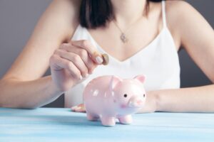 Female putting a pound coin into a pink piggybank