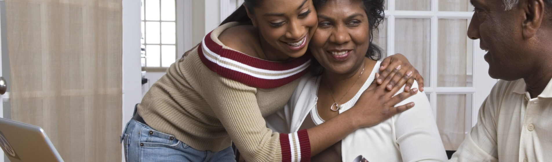 Young Person hugging her mother whilst looking at her father- everyone is happy