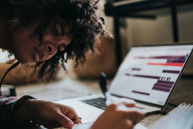 Young female with headphones in writing with laptop open
