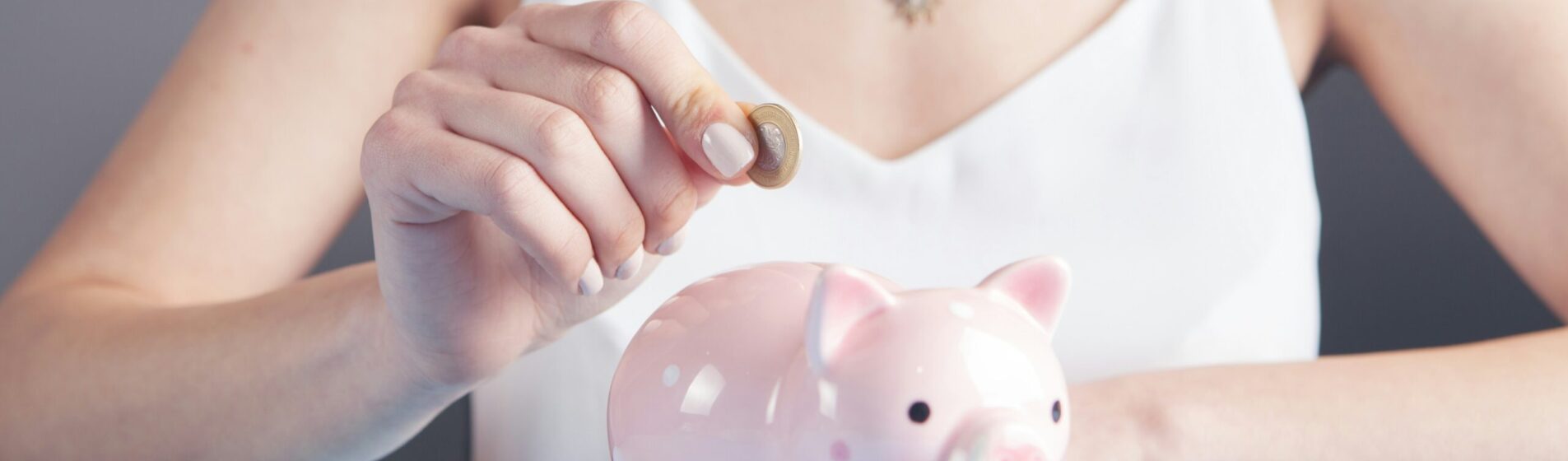 Female putting a pound coin into a pink piggybank